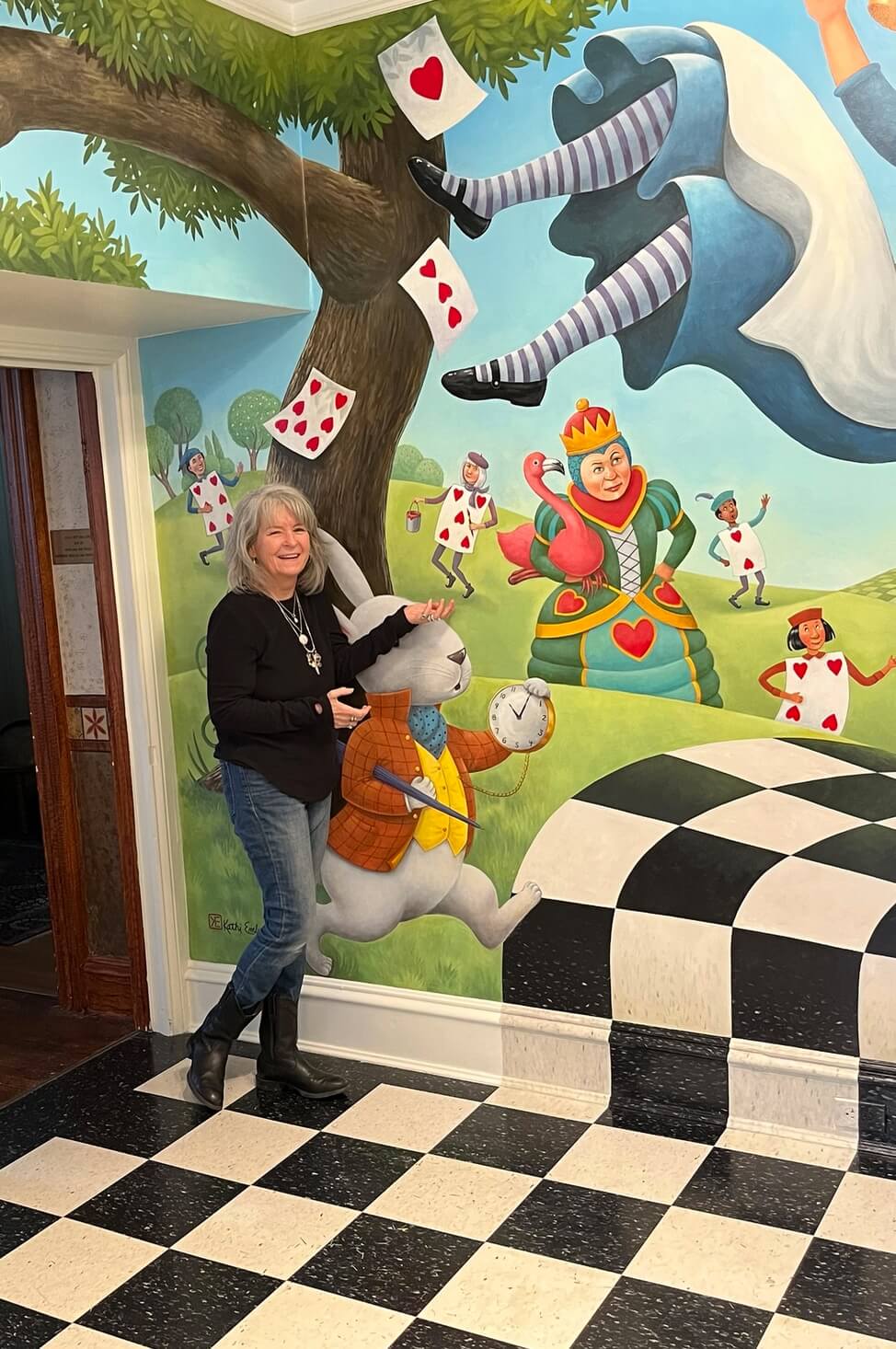 Artist Kathi Ember stands with her "Alice in Wonderland" mural